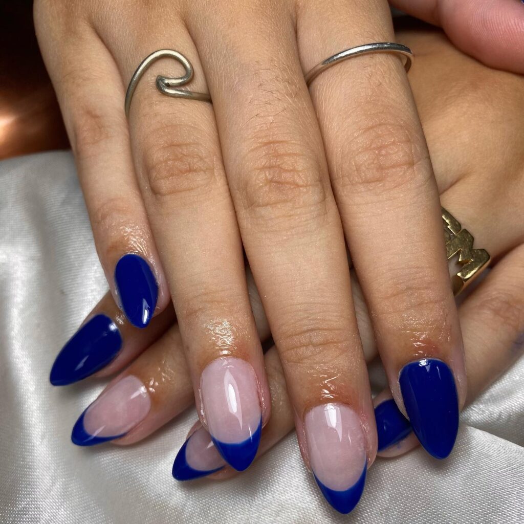 A hand with nails bearing a clear base and striking blue French tips, paired with silver rings for a contemporary look.