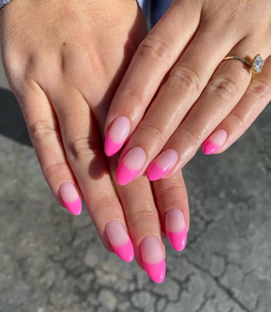 Elegant hand with almond-shaped nails featuring a pink ombré design, transitioning from a vibrant tip to a clear base.