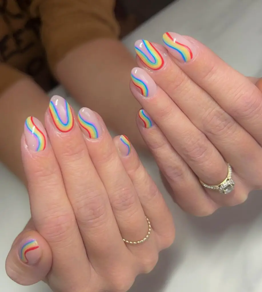 Hands with a colorful swirl pattern nail art in rainbow hues on a white base, perfect for a fun and vibrant look.