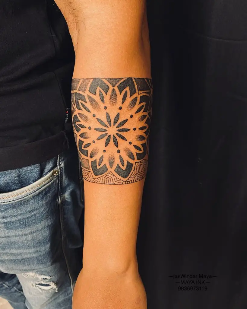 A forearm tattoo of a mandala with a complex network of radiating shapes and patterns.
