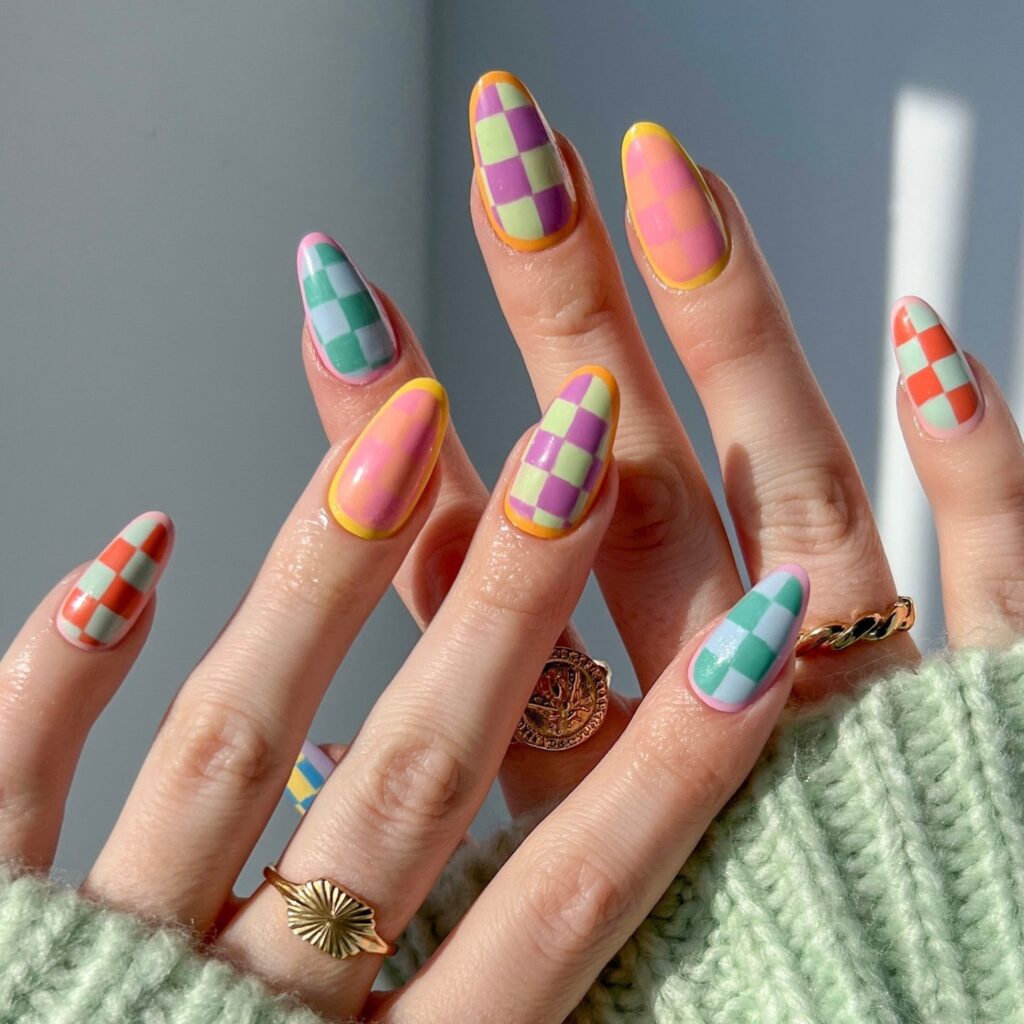 Hands with nails painted in pastel checkered patterns, combining shades of yellow, pink, and teal for a playful, modern look.