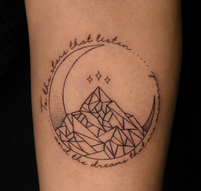 A calf tattoo featuring geometric mountains within a crescent moon, encircled by an inspirational quote.