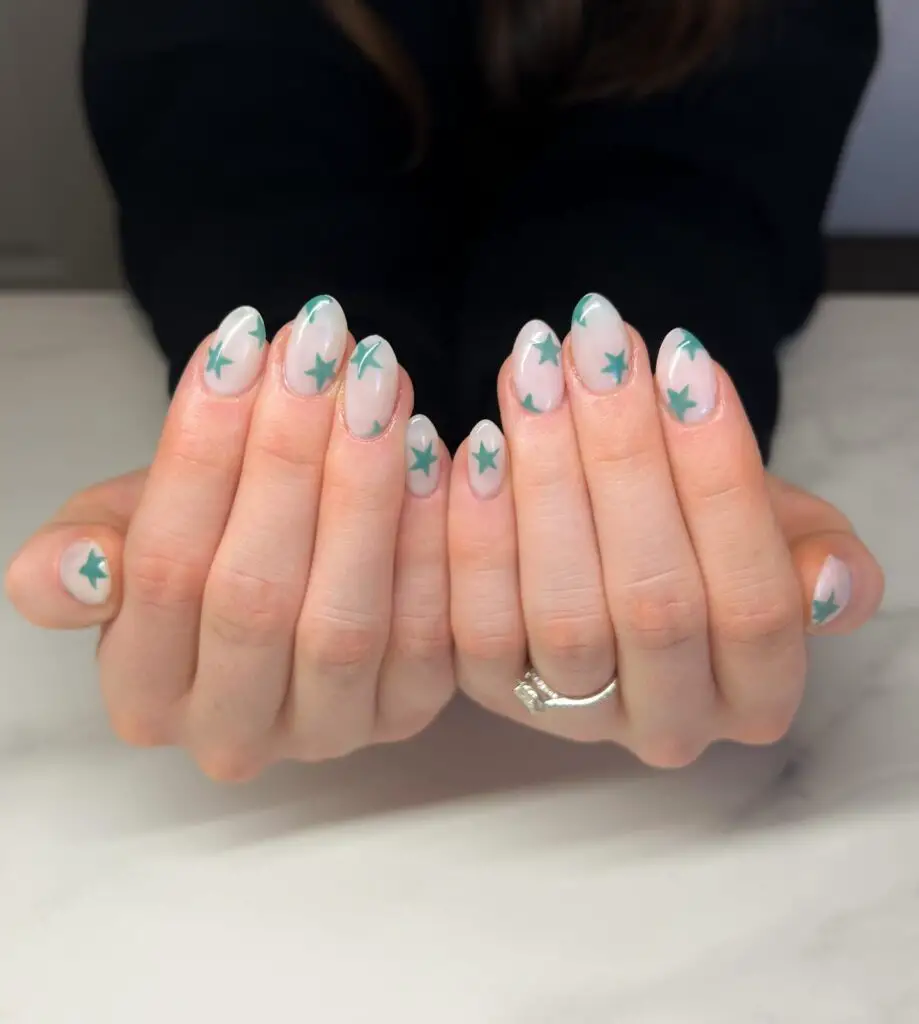 A set of neatly manicured nails with a sheer base, decorated with mint green stars for a whimsical and celestial-inspired nail design.