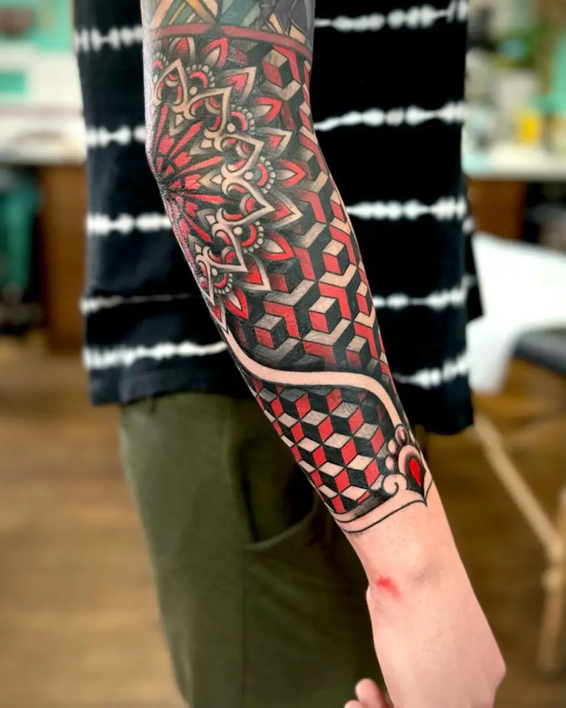 An arm with an elaborate geometric sleeve tattoo incorporating hexagonal shapes and vibrant red and black shading, demonstrating intricate linework and shading technique.