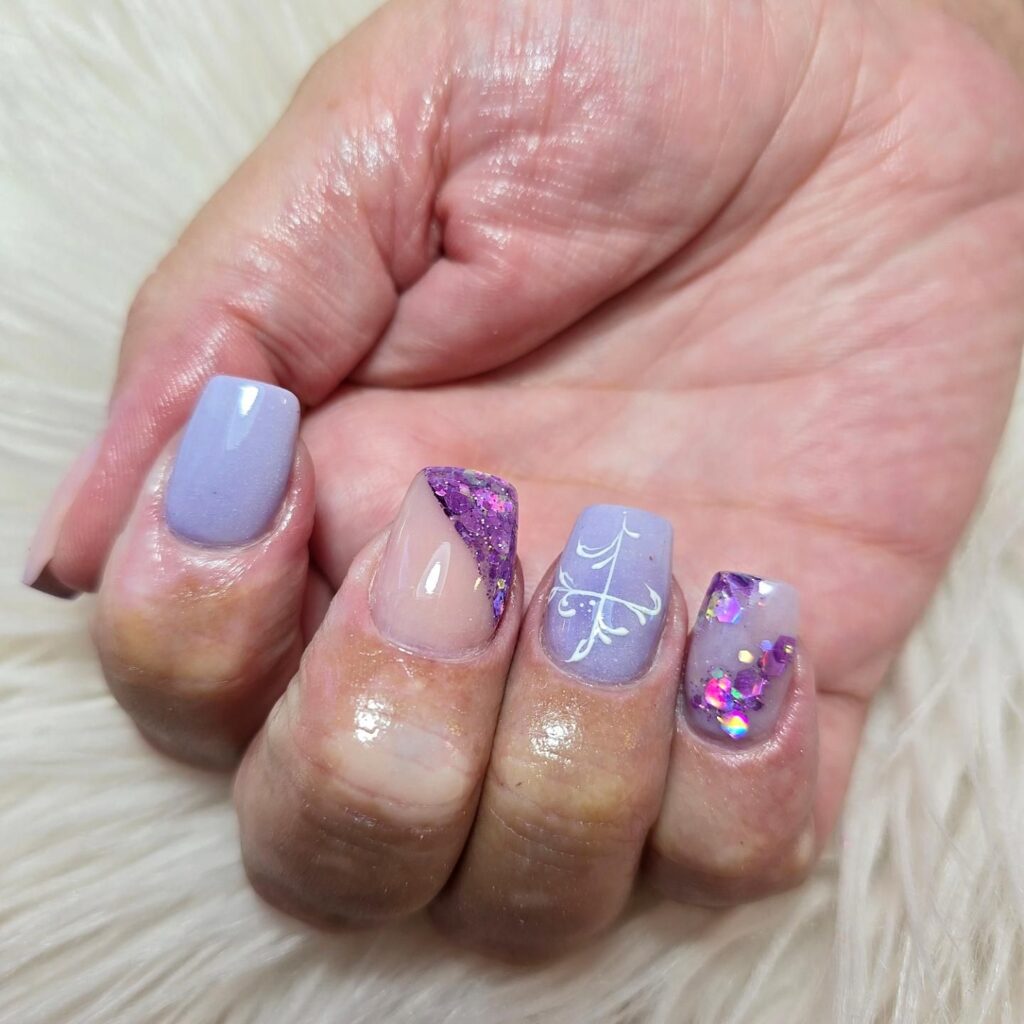 A hand with a mix of matte lavender, glittery purple, and embellished nails, providing inspiration for spring nail designs with varied textures and styles.