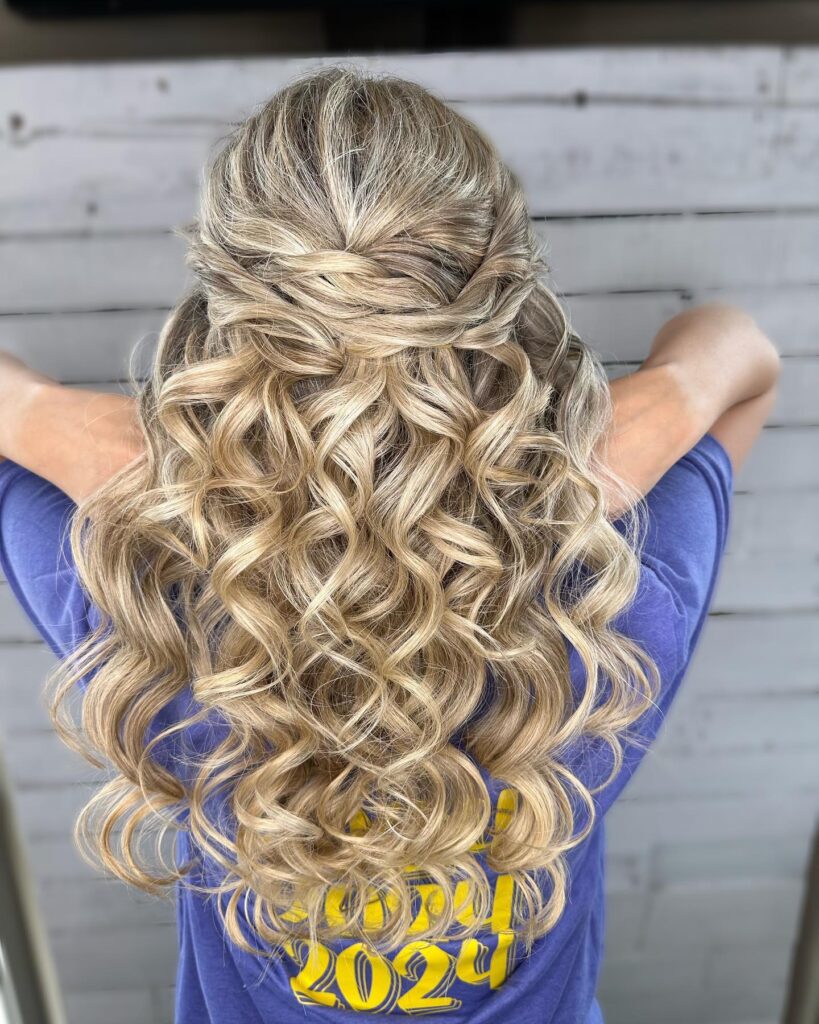 Back view of a woman's half-up hairstyle with twists leading into voluminous, curly blonde hair, styled for a glamorous prom appearance.