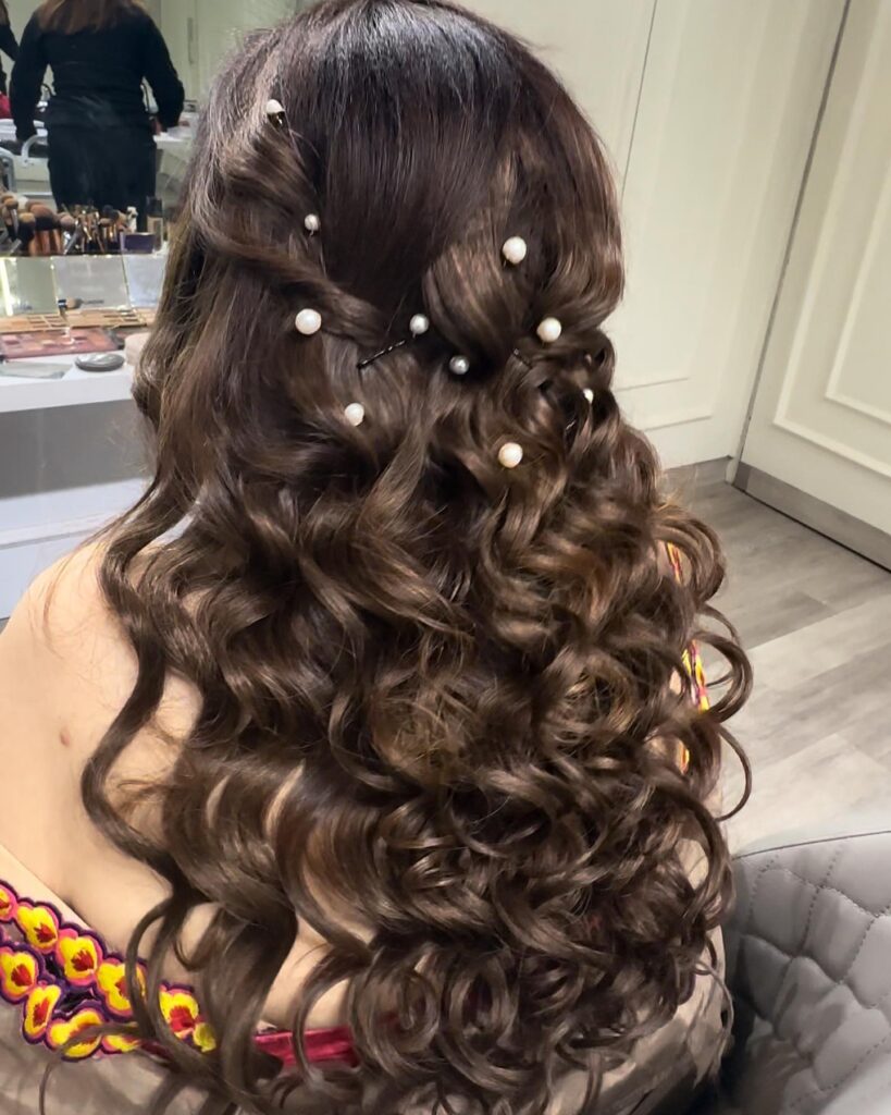 Rich brunette curls with sections twisted and secured with pearl pins for an elegant prom hairstyle.