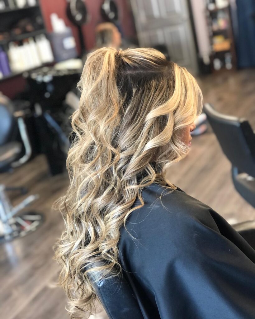 Voluminous half-up curls with honey blonde highlights, perfect for a chic and modern prom look.