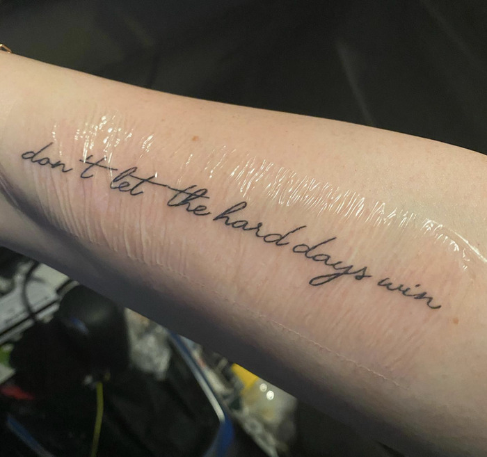 A forearm tattoo with the phrase "don't let the hard days win," in delicate script, symbolizing resilience and hope.