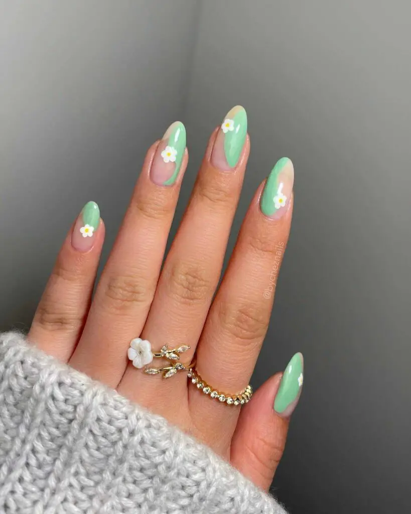 Hand with nails coated in mint green and adorned with subtle white flowers, reflecting a fresh and minimalistic approach to spring nail art.