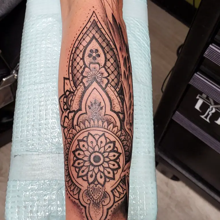 A detailed forearm tattoo of a mandala with concentric patterns and a lotus center, showcasing expert dotwork and line art.