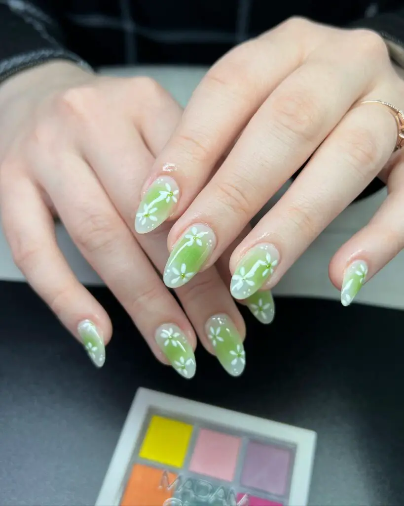 Almond-shaped nails with a soft green gradient and white floral designs, reminiscent of a blooming spring garden.
