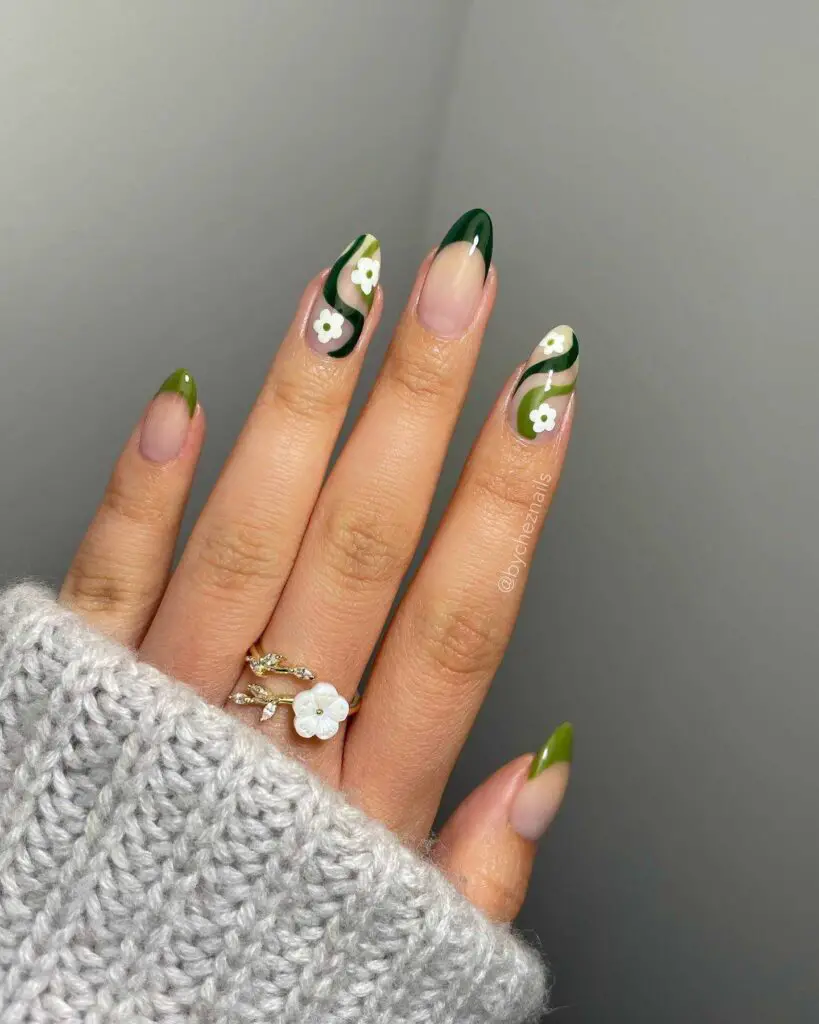 A hand displaying nails with deep green tips and white blossom designs, capturing the essence of spring's blooming greenery.