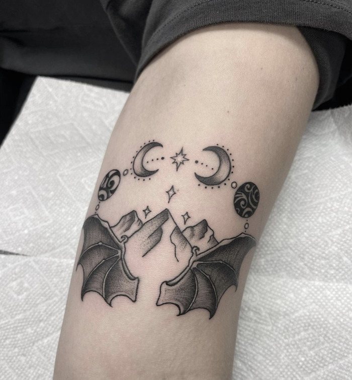 A tattoo of mountains and bats with crescent moons and stars, symbolizing a blend of earthly and celestial realms.