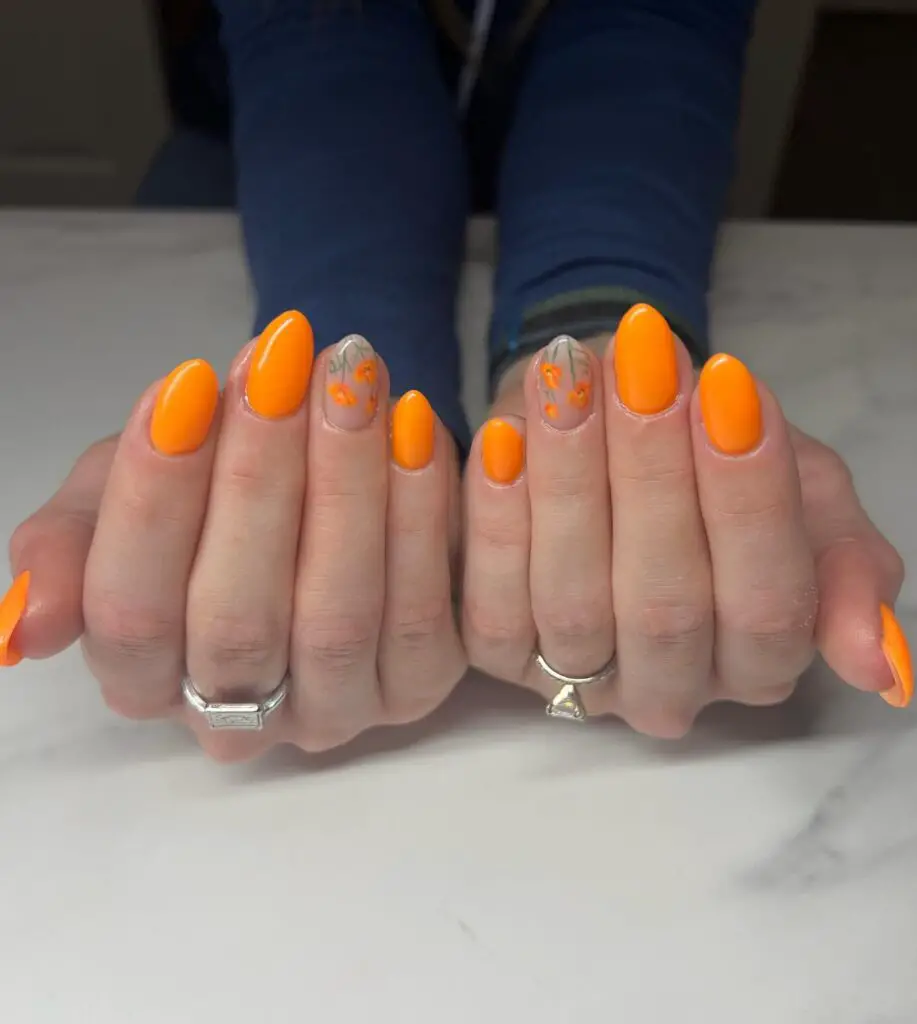 A bright and summery nail look featuring vibrant tangerine nails with two accent nails that have a clear base and delicate orange floral details.
