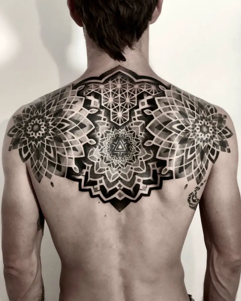 A symmetrical back tattoo featuring a large central mandala and radiating geometric patterns extending over the shoulders.