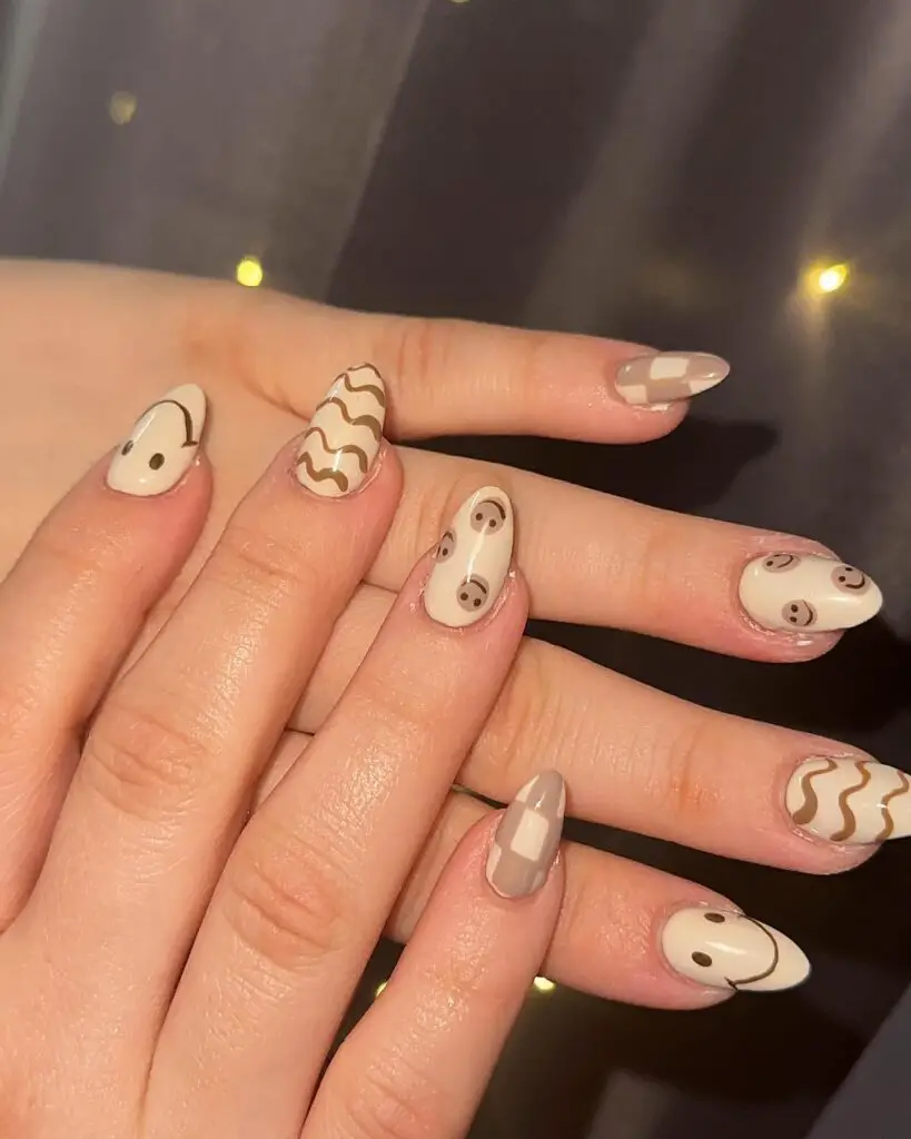 A hand displaying nails painted with coffee-inspired designs, including latte art patterns in creamy beige tones.