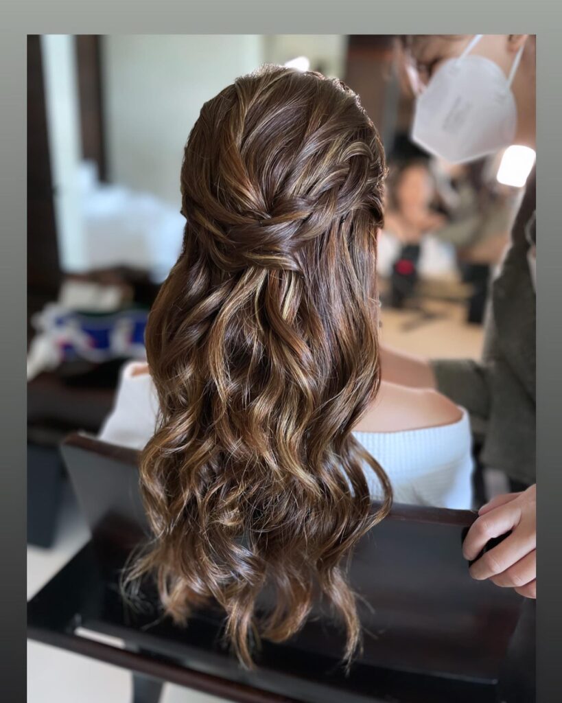 Elegant twists lead into waves on brunette hair with highlights, styled for a stunning prom look.