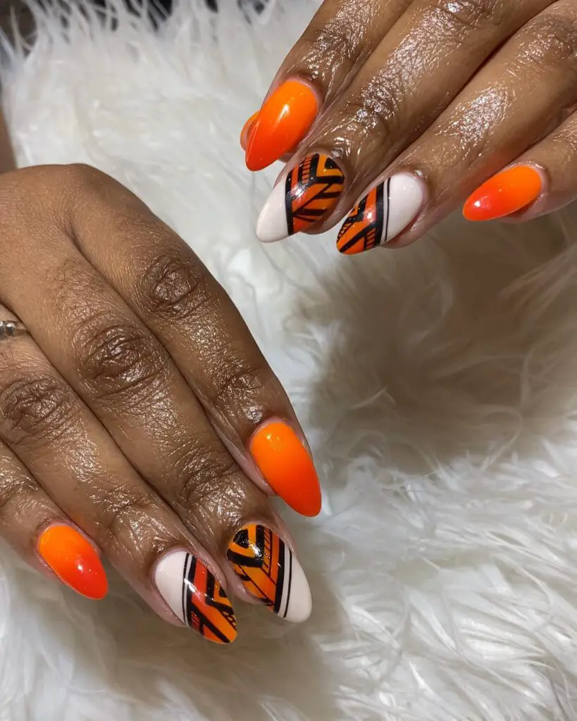 Long, stylish nails painted with neon orange and accented with bold black tiger stripes on a white base, creating a daring and exotic look.