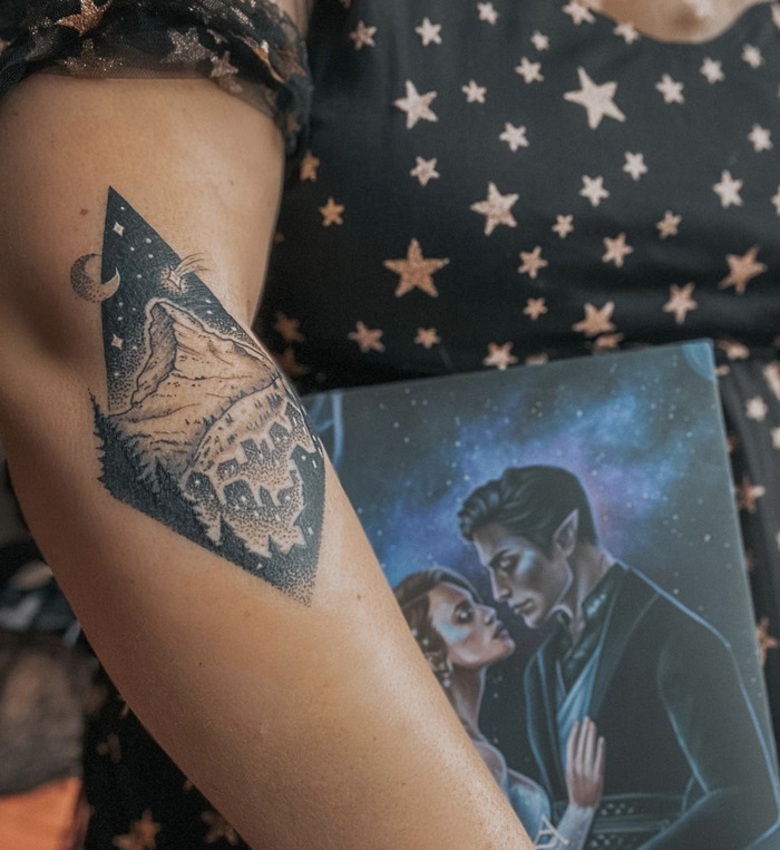 A tattoo of a mountain under a moon and stars within a triangular frame, conveying the enchantment of the night.