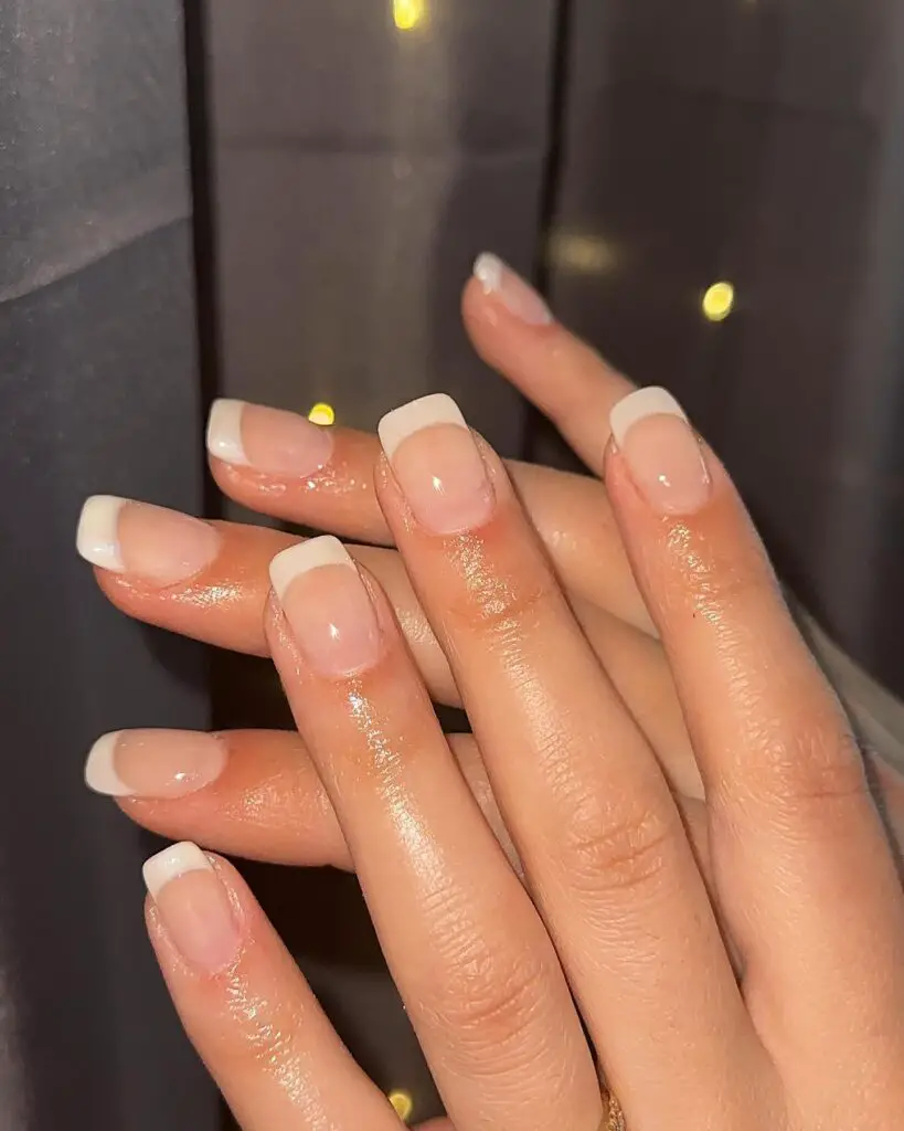 Elegant hands with a classic French manicure featuring white tips on a natural, shiny nail base.
