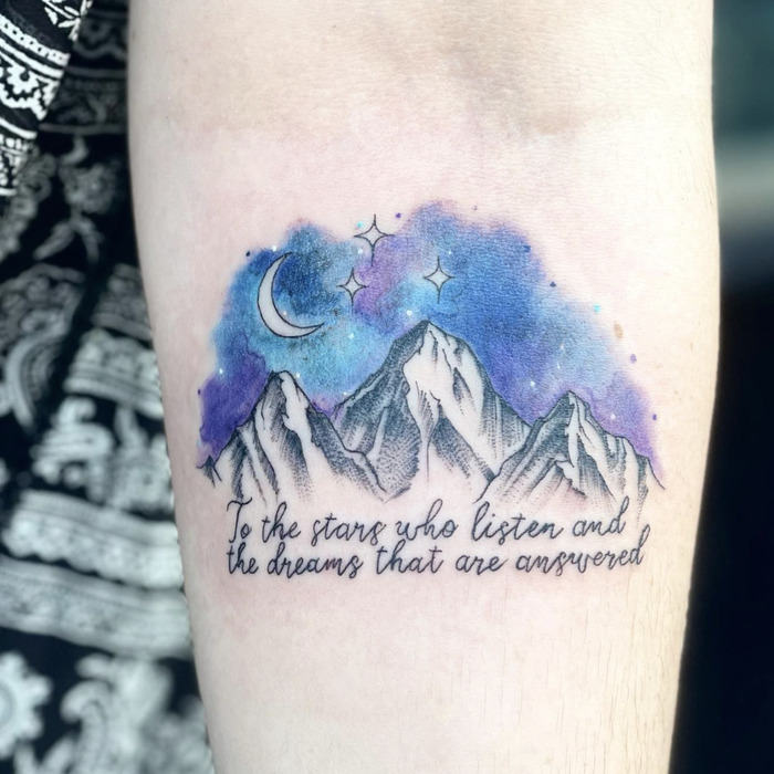 A calf tattoo with mountains, a moon, and stars in watercolor style, paired with an inspiring quote.