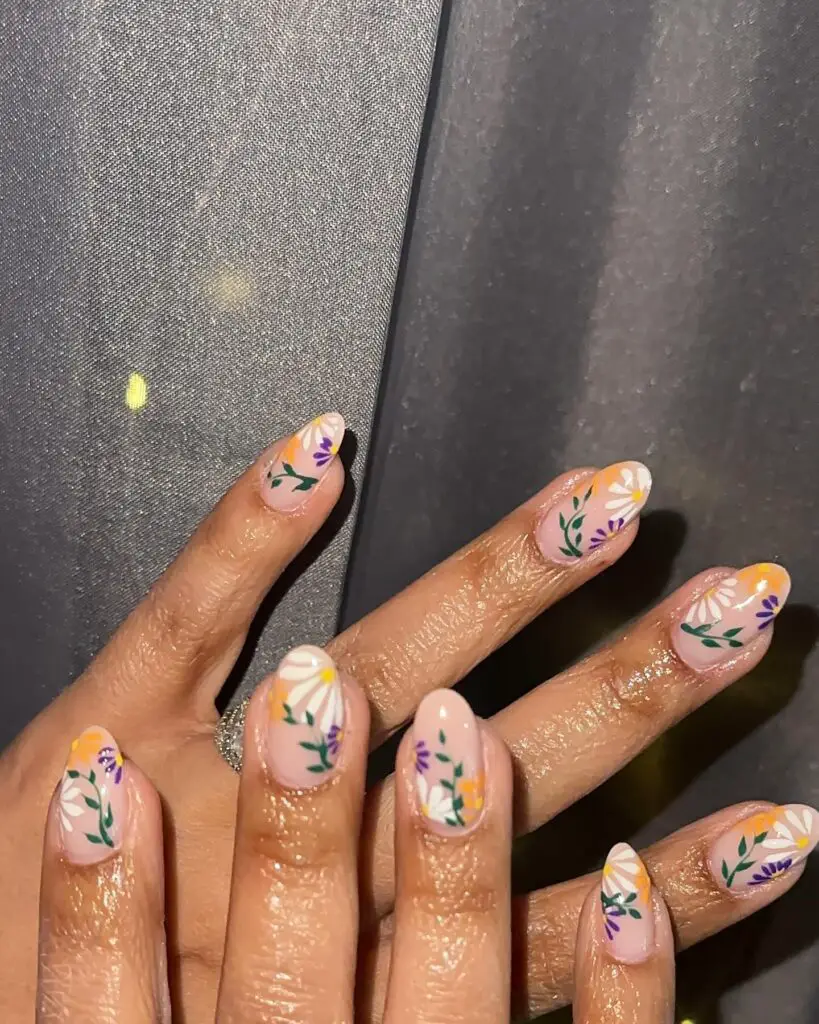 Hands with nails painted in a pastel base adorned with delicate floral patterns in lavender, orange, and white.