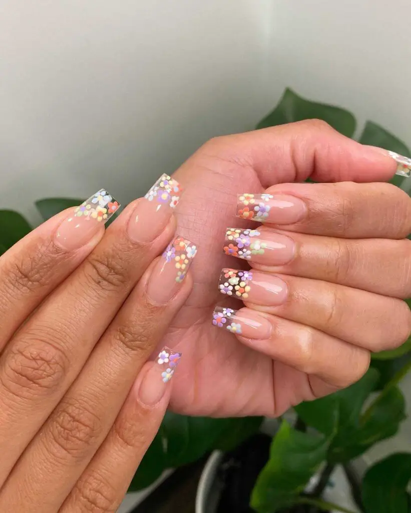 Nails adorned with a nude base and vibrant confetti flower patterns, reminiscent of a festive spring flowerbed.