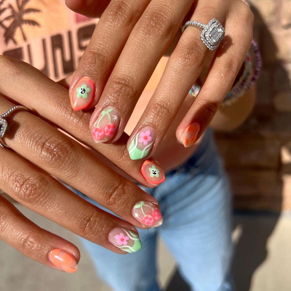 Hands with nails painted in a serene blue color, detailed with delicate orange and green floral patterns on clear nail tips.