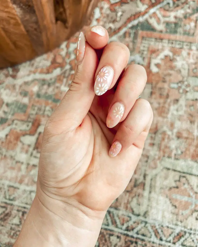 A hand with an elegant ivory manicure, detailed with subtle white floral designs for a touch of timeless grace.
