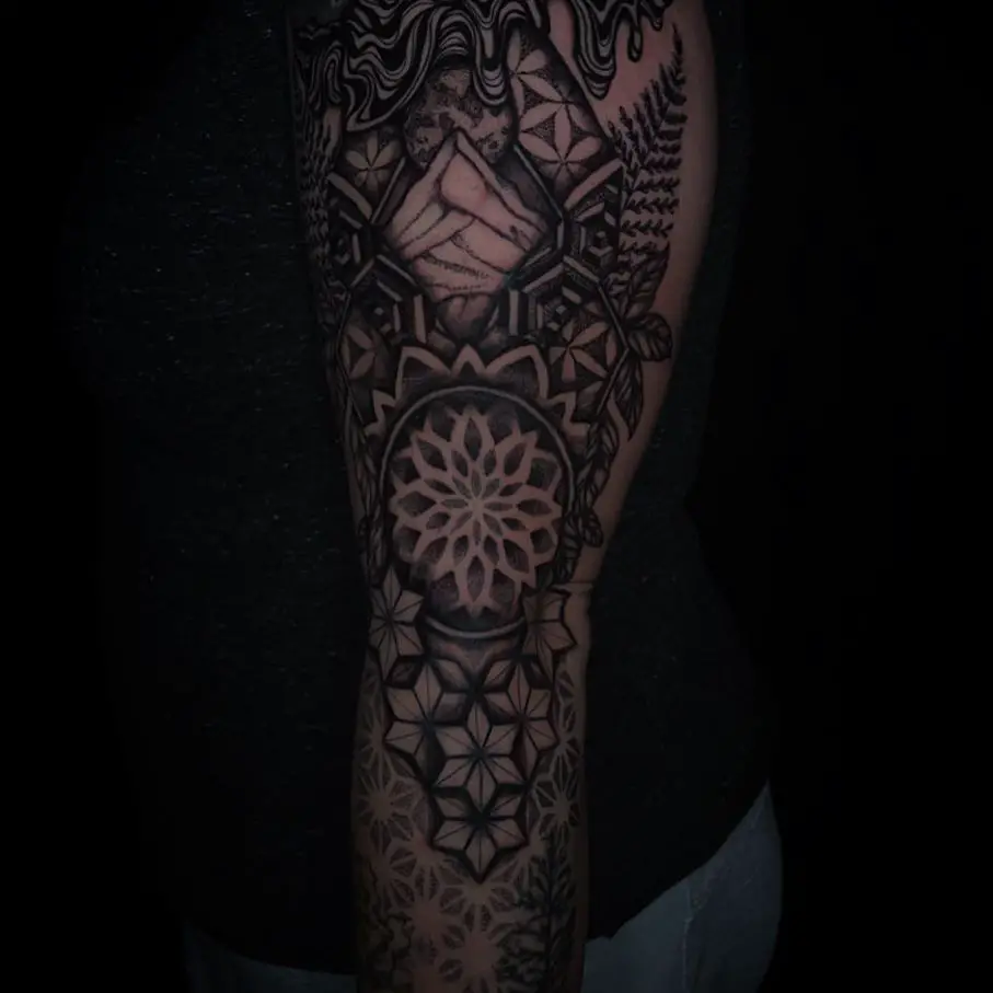 An arm sleeve tattoo blending dark shading with natural and geometric motifs, such as mandalas and stars.