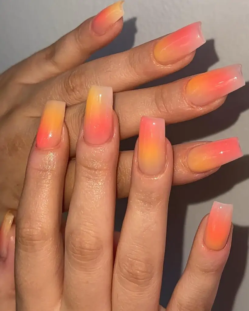 A hand with nails displaying a smooth gradient from yellow to pink, reminiscent of a serene sunset sky.