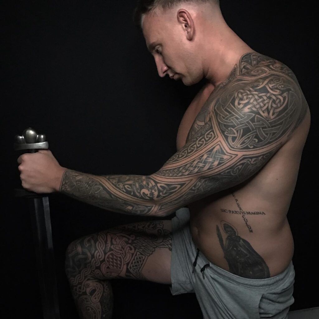 An extensive black and gray Viking-themed tattoo, covering an arm and a leg with mythological elements and knotwork.