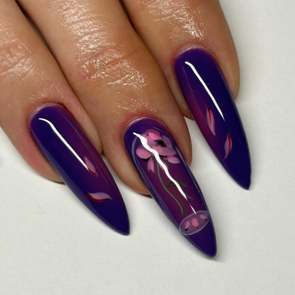 A hand displaying stiletto nails with a deep purple polish and a detailed white floral design, perfect for articles about sophisticated spring nail art trends.