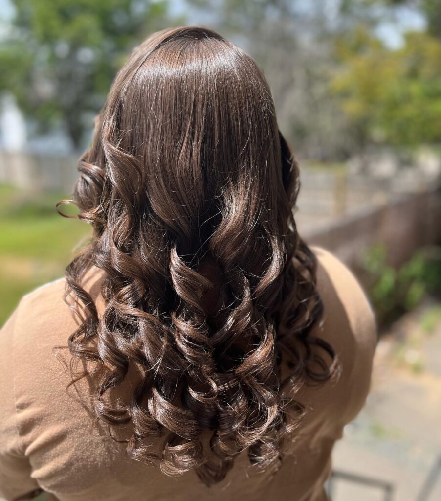 A woman's hair styled into shiny, bouncy curls of a deep chocolate brown shade, ideal for a sophisticated prom night hairstyle.