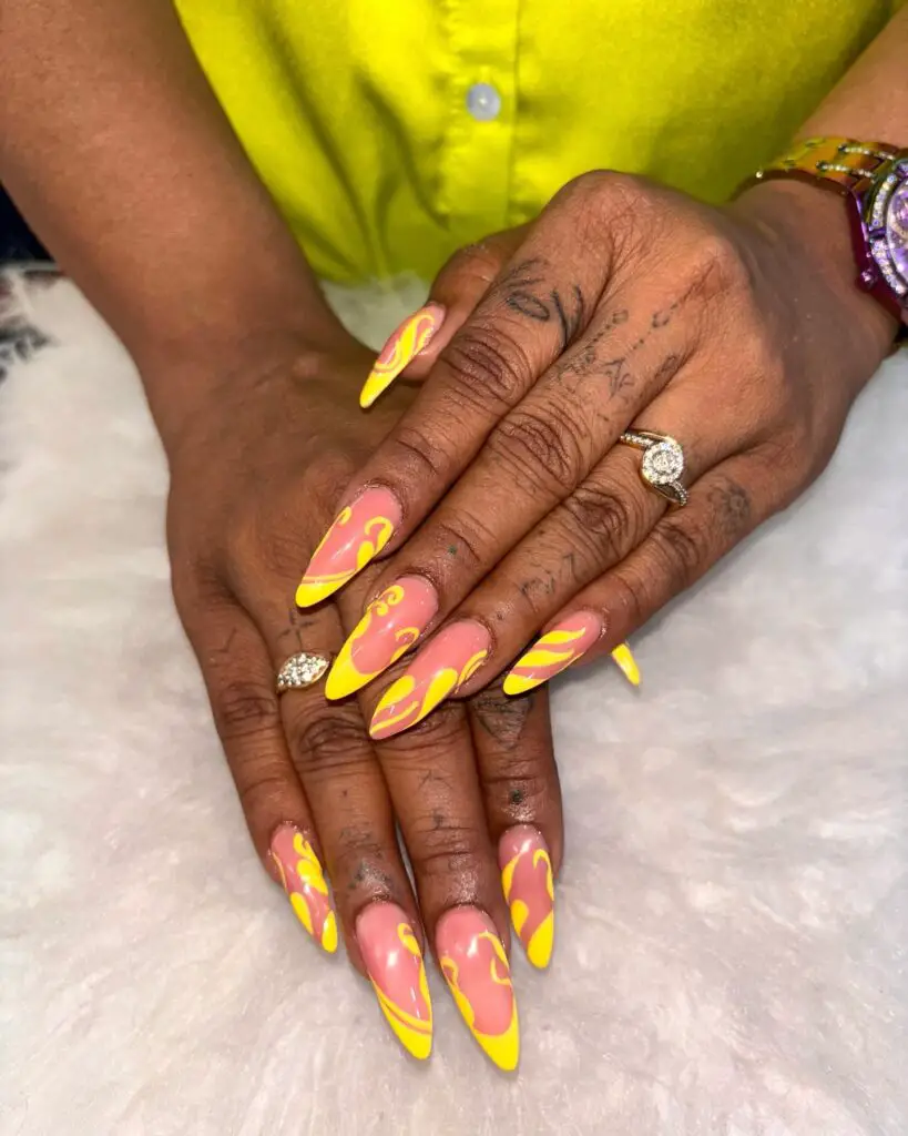 Long stiletto nails with a bright yellow base and pink swirl patterns, making a bold statement on the wearer's hands.