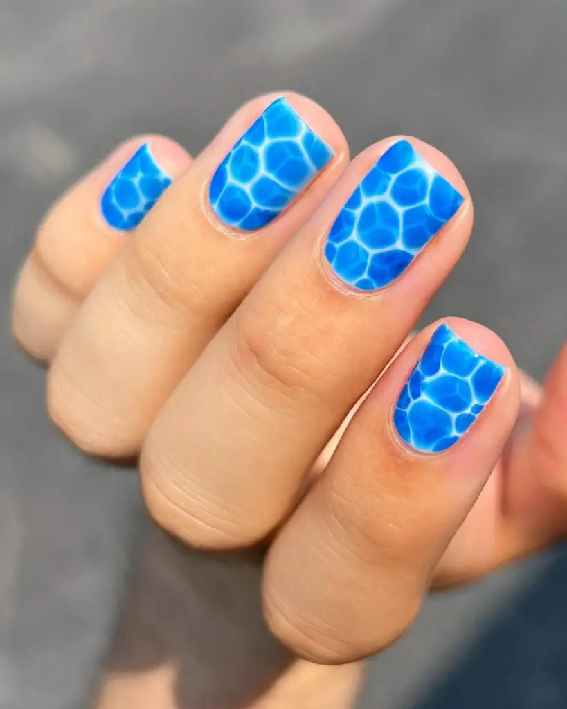 Close-up of nails with a vibrant blue honeycomb design, capturing the essence of the ocean's depth.