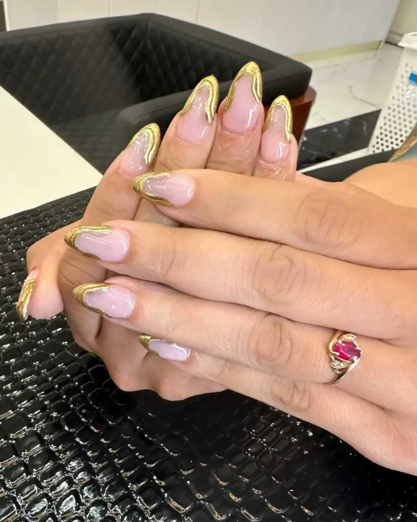 Nails with a lustrous nude base and rich golden French tips, offering an elegant and luxurious manicure style.