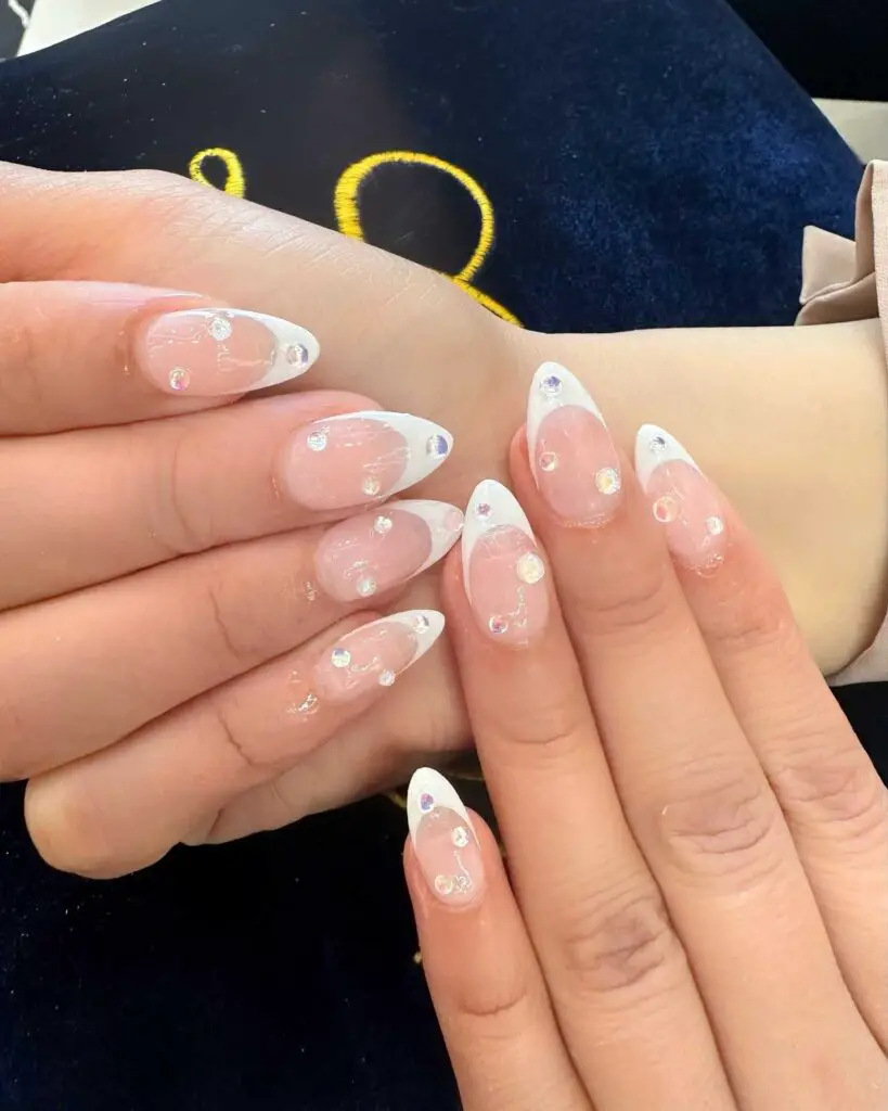 A hand featuring nails with a clear base and tasteful crystal embellishments, creating a minimalist yet charming manicure.