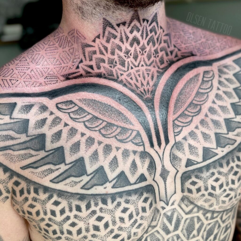 A detailed black and pink mandala tattoo on a person's neck and upper shoulders with intricate geometric patterns.