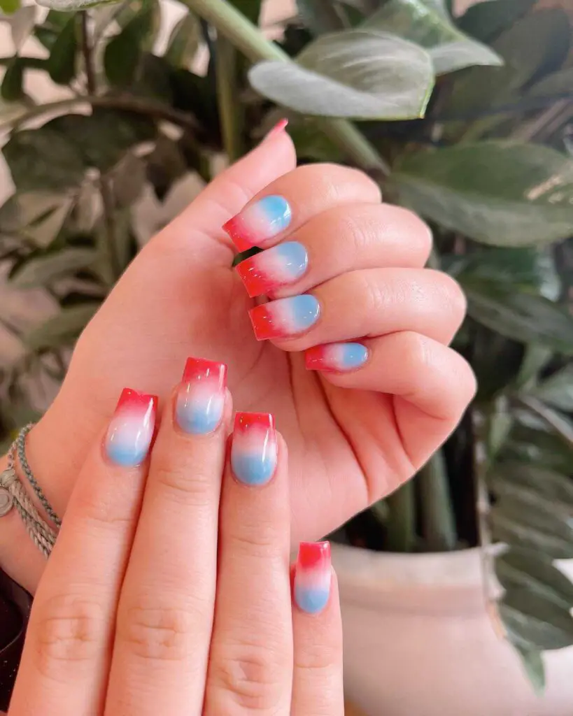 A hand with nails showcasing a stunning red to blue gradient, reminiscent of a fiery sunset sky.