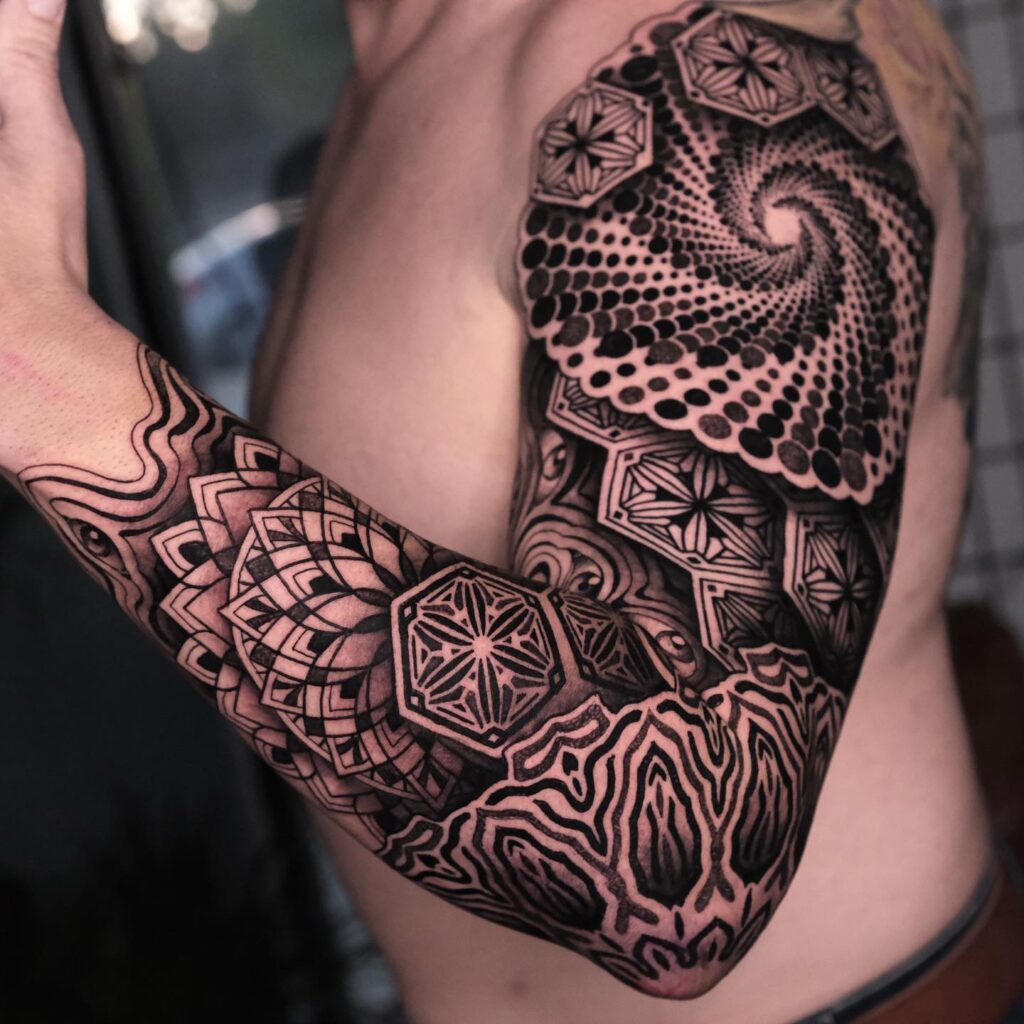 A bold black spiral mandala tattoo on a person's upper arm, featuring a mix of geometric and organic patterns.