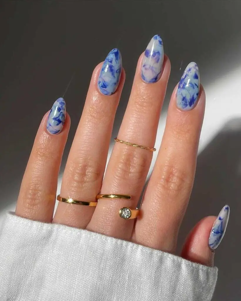 A hand with nails featuring a blue and white marble effect, giving the appearance of delicate and artistic porcelain.