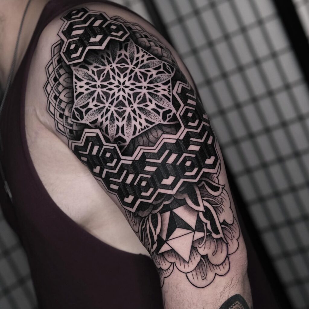A geometric mandala tattoo covering a person's shoulder and upper arm with a combination of sharp and soft patterns in black ink.