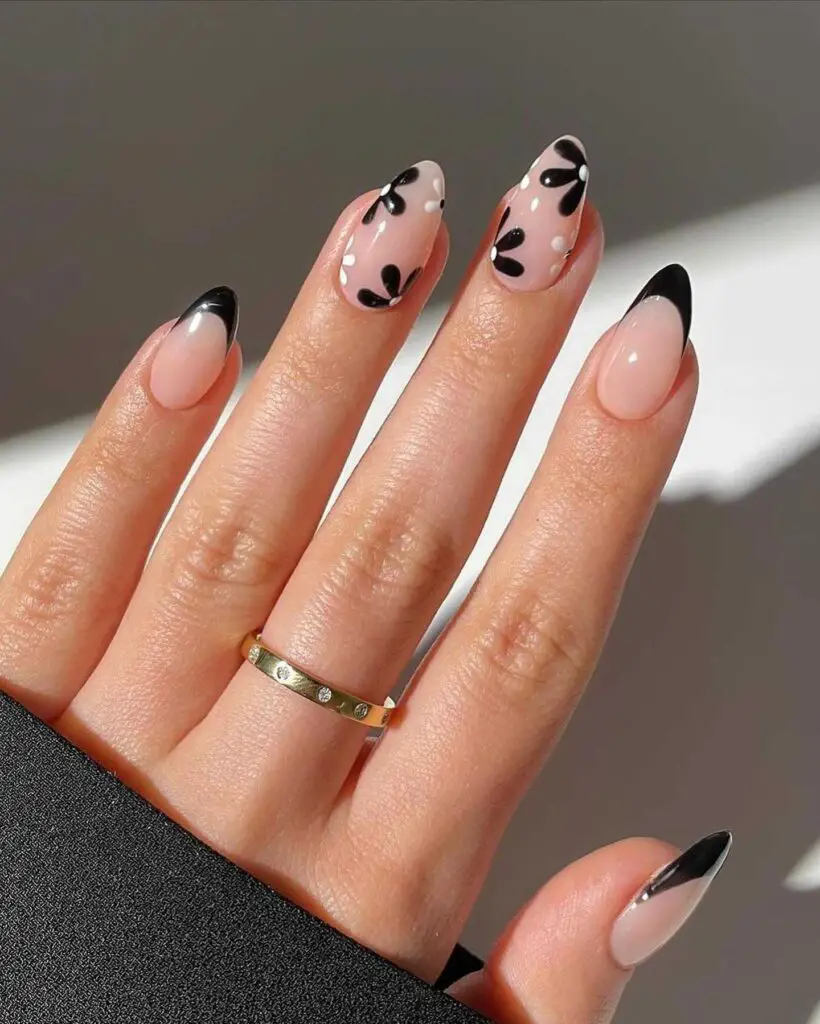 A hand with nails featuring abstract black hearts at the tips and delicate white dot outlines, creating a modern twist on the French manicure.