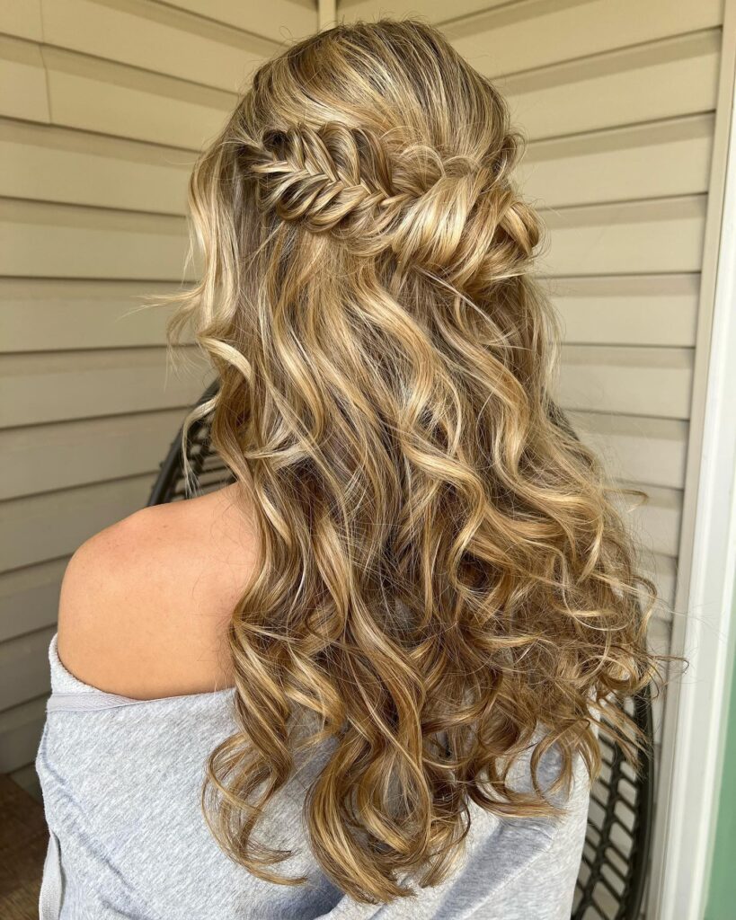 A woman's hairstyle featuring a twisted half-updo with intricate knotting and voluminous blonde curls, ideal for a refined and stylish prom look.