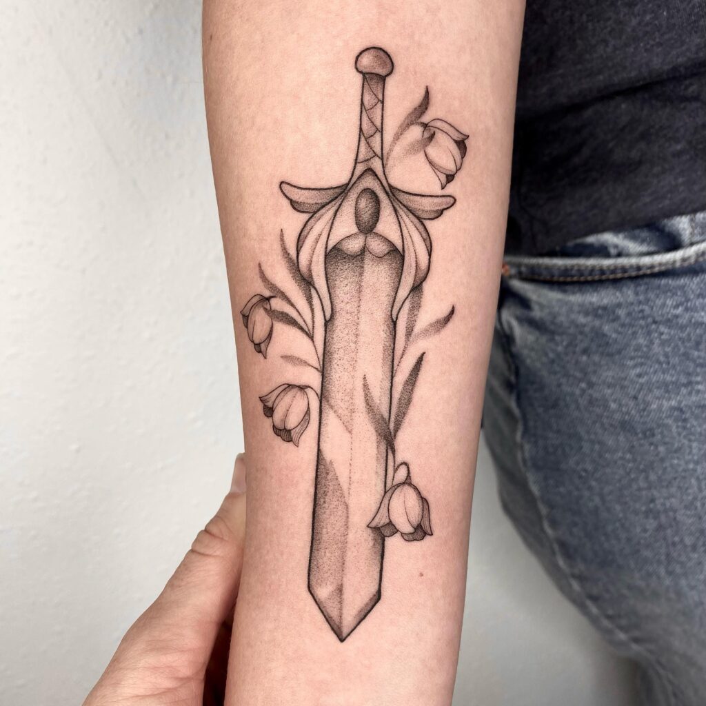 An arm tattoo featuring a sword encircled by blooming roses, signifying strength and beauty.