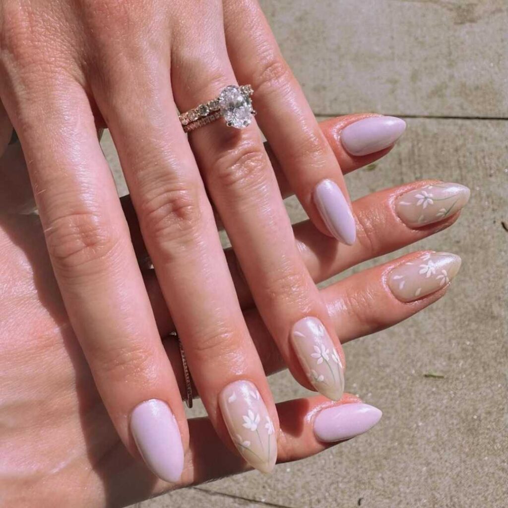 A hand displaying almond-shaped nails painted in petal pink with delicate white floral art, epitomizing soft, feminine elegance.