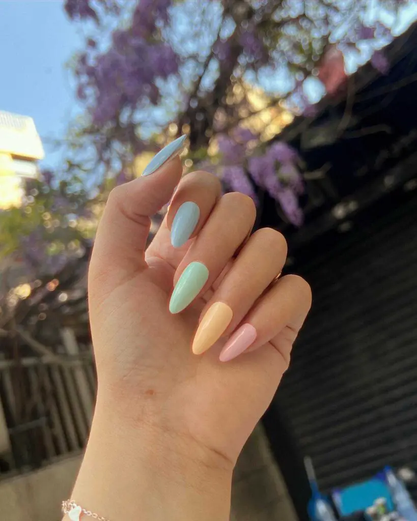 A hand with nails featuring a pastel gradient from sky blue to peach to pink, reminiscent of a serene springtime dawn.