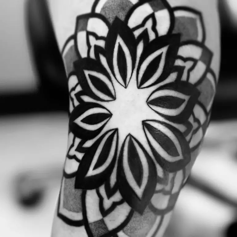 A black ink tattoo on the forearm showcasing a mandala with bold floral patterns.